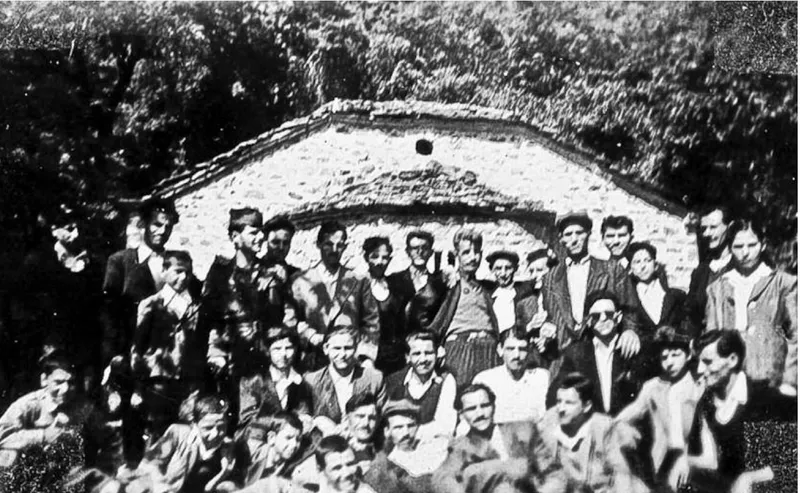 Μεγάλη ομάδα ανθρώπων μπροστά από ένα πέτρινο εκκλησάκι