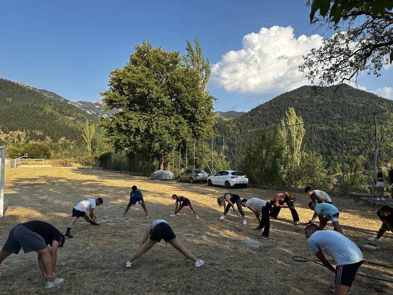 Προθέρμανση με διατάσεις στο γήπεδο του χωριού, κάτω από τα δέντρα και το βουνό